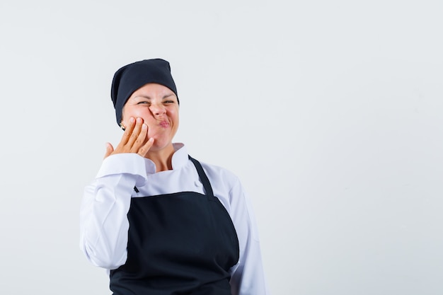 Female cook in uniform, apron suffering from toothache and looking uncomfortable , front view.