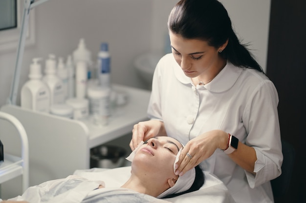 Female cosmetologist making facial treatment to a beautiful woma