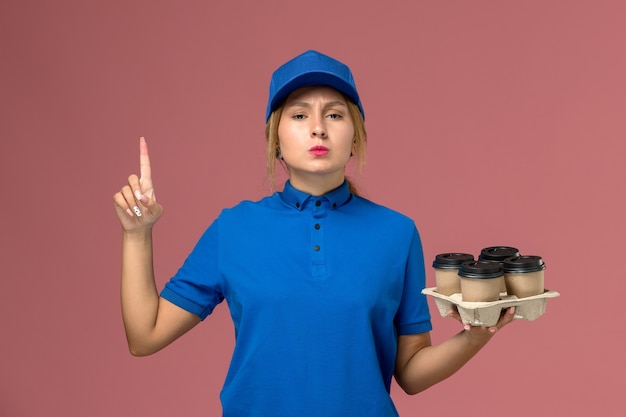 Free Photo female courier in blue uniform holding delivery cups of coffee with raised finger on pink, service worker uniform delivery