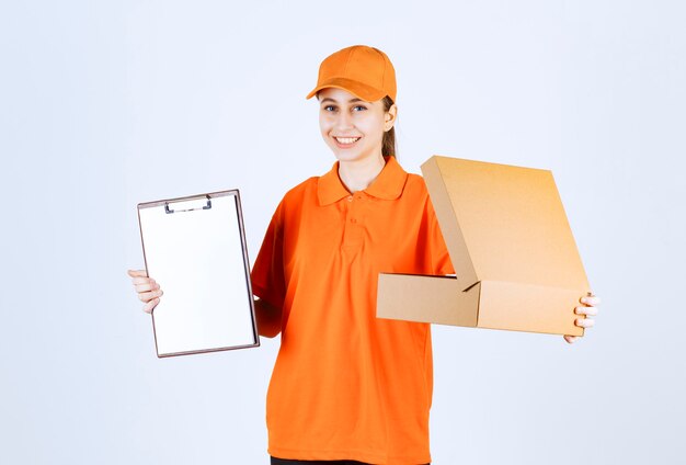 Female courier in orange uniform holding an open cardboard box and asking for a signature.