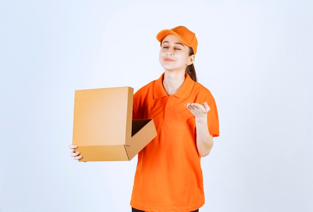 Female courier in orange uniform holding an open cardboard box and smelling the product inside.