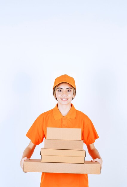 Free photo female courier in orange uniform holding a stock of cardboard parcels