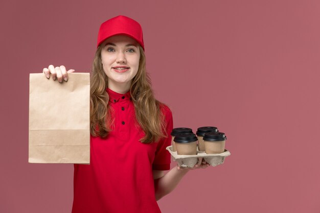 female courier in red uniform holding delivery food package with coffee cups on light pink, job uniform service delivery