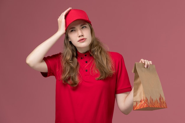 female courier in red uniform holding food package on light-pink, job uniform service worker delivery