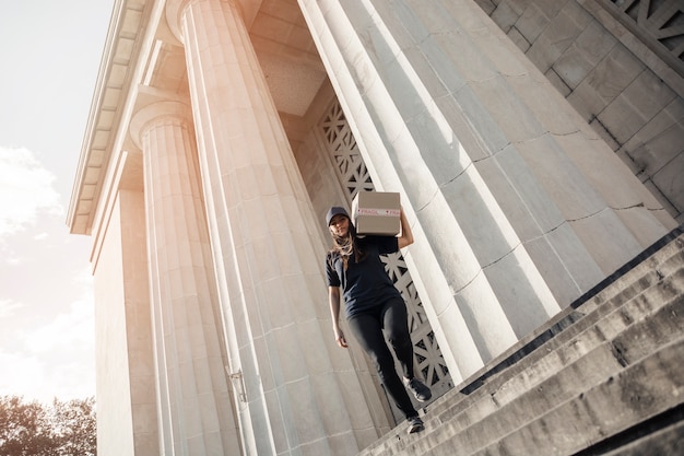 Free photo female courier walking on staircase with parcel