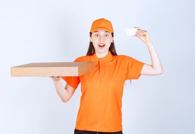 Female courier in yellow uniform holding a cardboard takeaway box and presenting her business card.