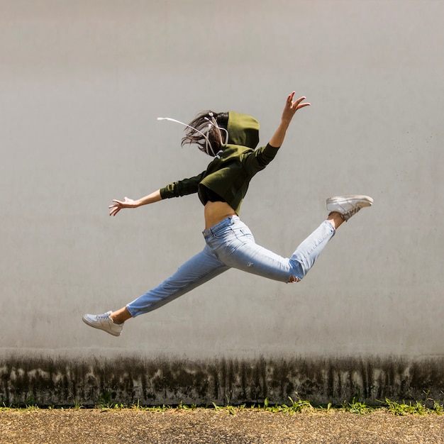 Free photo female dancer in hood jumping against wall