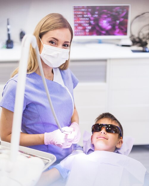 Female dentist standing near boy wearing safety protective glasses