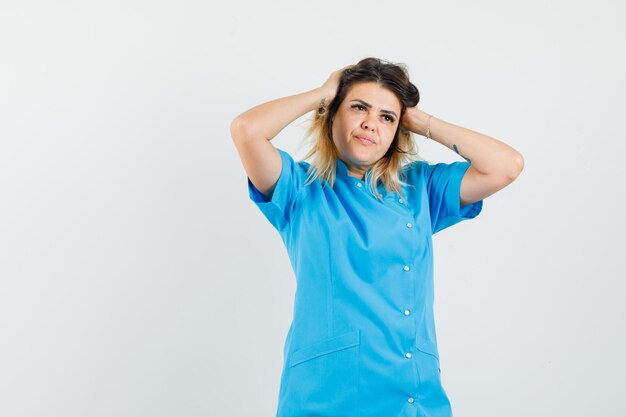 Female doctor in blue uniform clasping head with hands and looking pensive