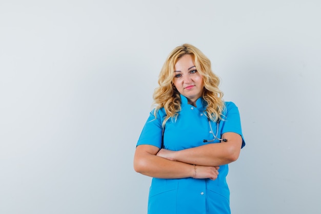 Female doctor in blue uniform keeping arms crossed and looking pensive space for text