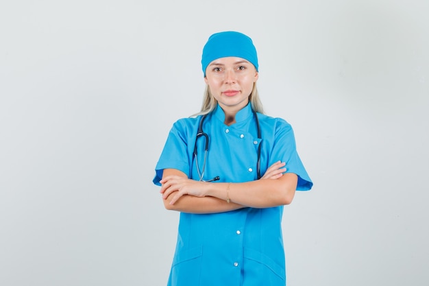 Female doctor in blue uniform smiling with crossed arms and looking hopeful 