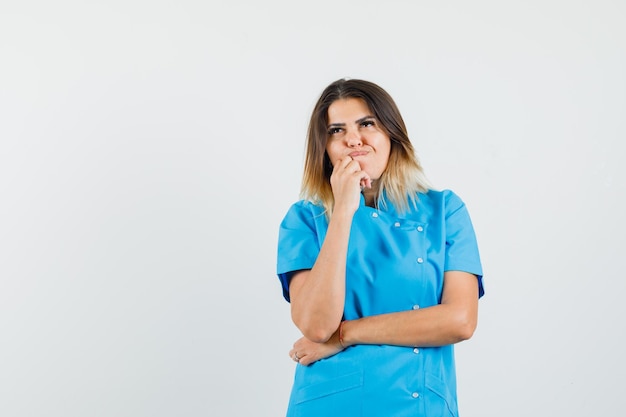 Female doctor in blue uniform standing in thinking pose and looking indecisive