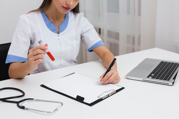 Female doctor hand writing a report and holding a blood sample