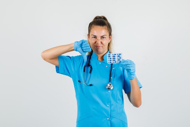 Female doctor holding capsules with thumb down in blue uniform