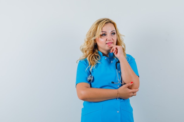 Free photo female doctor holding hand on chin while looking aside in blue uniform and looking focused. space for text