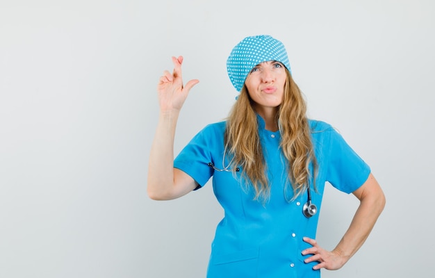 Free photo female doctor keeping fingers crossed while looking up in blue uniform and looking hopeful.