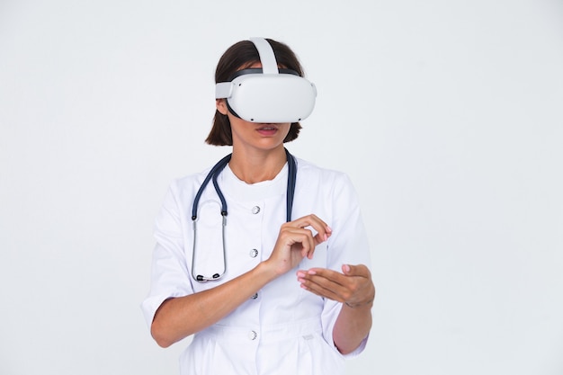 Female doctor in lab coat on white  isolated, wearing virtual reality glasses touch air