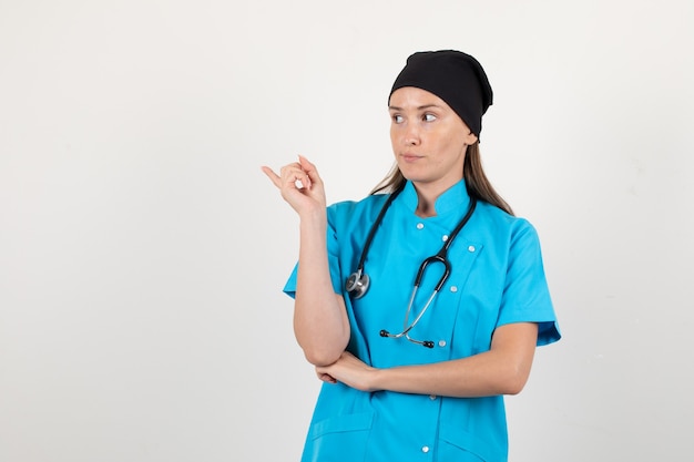 Female doctor looking aside and pointing finger away in uniform front view.