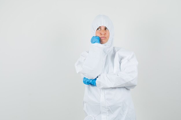 Female doctor looking up in protection suit, gloves and looking thoughtful.