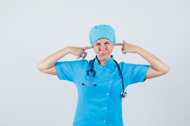 Free photo female doctor plugging ears with fingers in blue uniform and looking annoyed. front view.