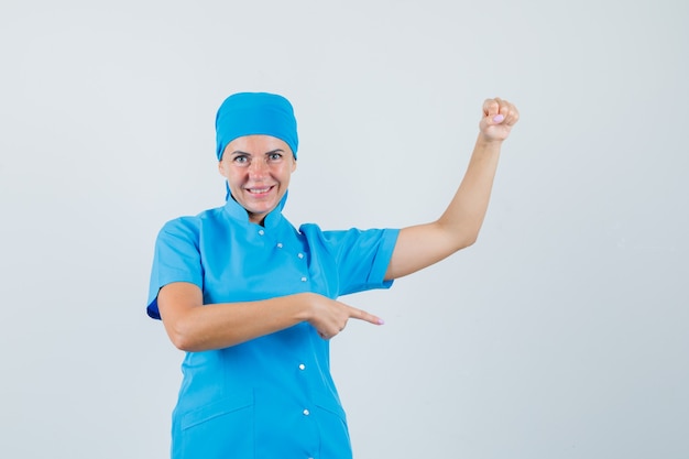 Female doctor pointing aside, pretending to hold something in blue uniform front view.