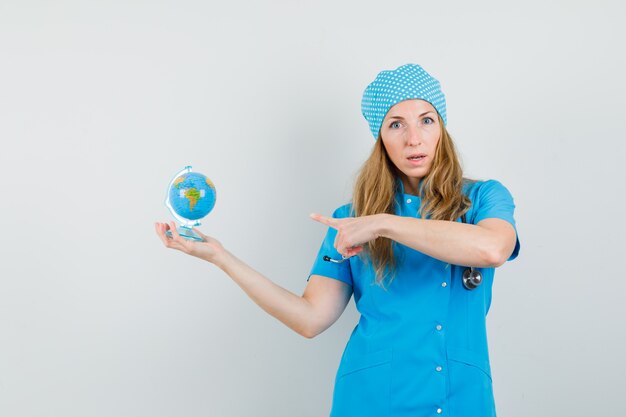 Female doctor pointing at globe in blue uniform 