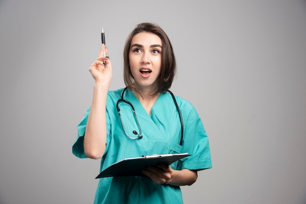 Female doctor pointing at something on gray background. High quality photo