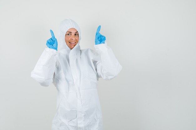 Female doctor pointing up in protective suit, gloves and looking happy