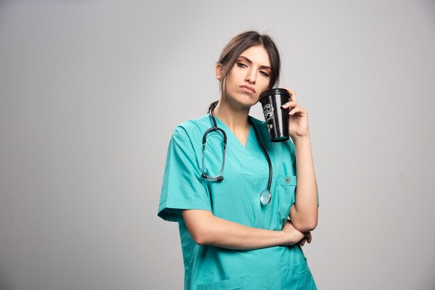 Female doctor posing with cup of coffee on gray