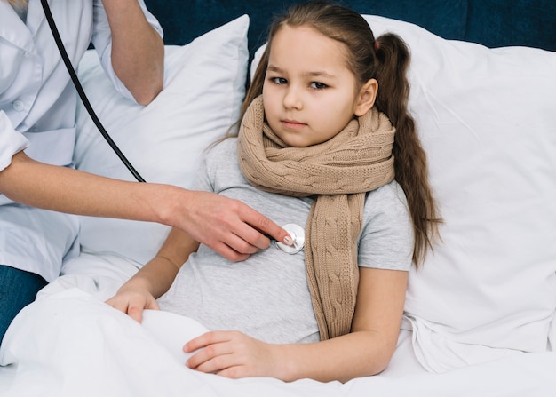 Free photo female doctor's hand examining girl lying on bed with stethoscope