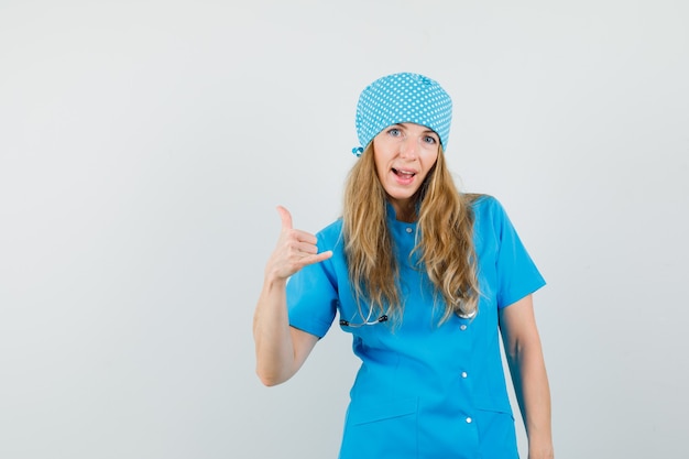 Female doctor showing phone gesture in blue uniform and looking confident 