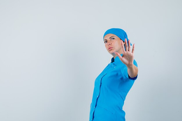 Female doctor showing stop gesture in blue uniform and looking anxious , front view.