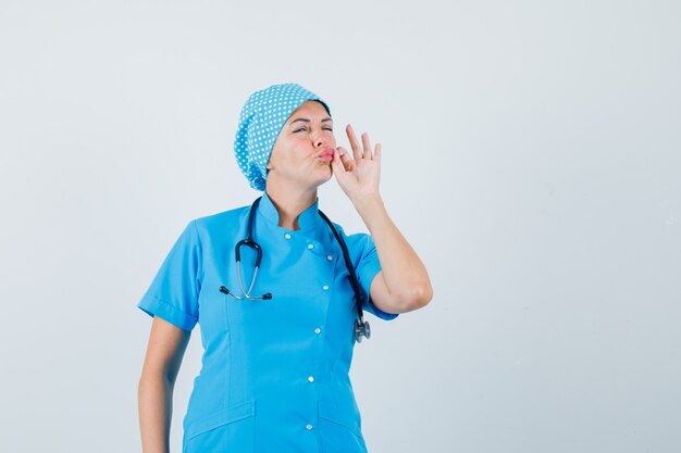 Female doctor showing zip gesture in blue uniform and looking careful , front view.