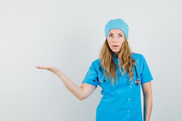 Female doctor spreading palm aside in blue uniform and looking puzzled 