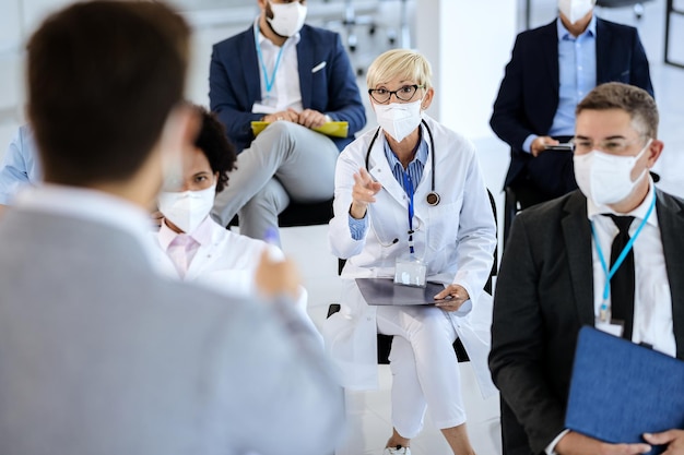 Free photo female doctor talking to presenter while attending a seminar during coronavirus epidemic