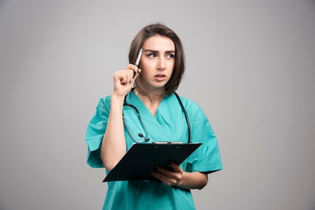 Female doctor thinking about patients on gray wall.