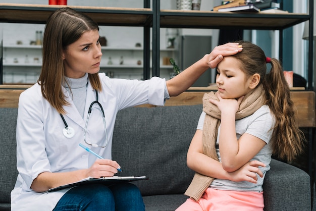 Female doctor touching the sick girl's forehead suffering from cold and fever