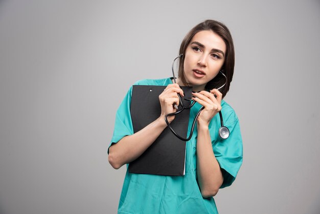 Female doctor using stethoscope on gray wall.