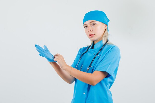 Female doctor wearing medical gloves in blue uniform and looking serious 