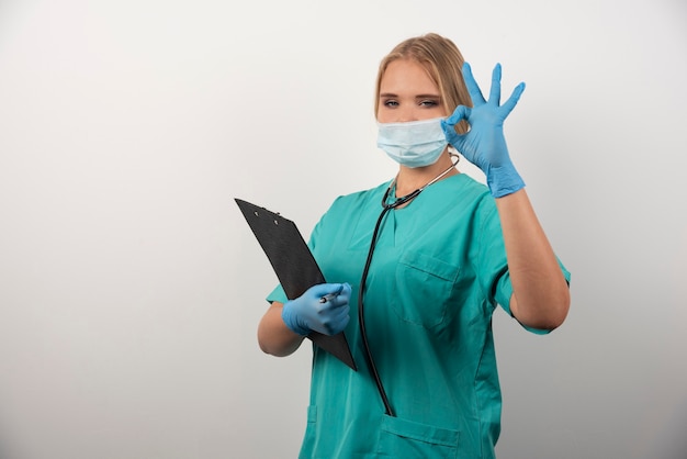 Female doctor with clipboard showing ok gesture.