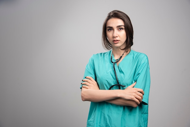 Female doctor with stethoscope standing on gray wall.