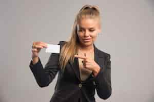 Free photo female employee in black suit presenting her business card and pointing at it.