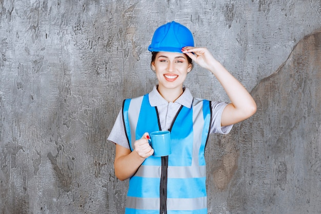 Free Photo female engineer in blue uniform and helmet holding a blue tea cup