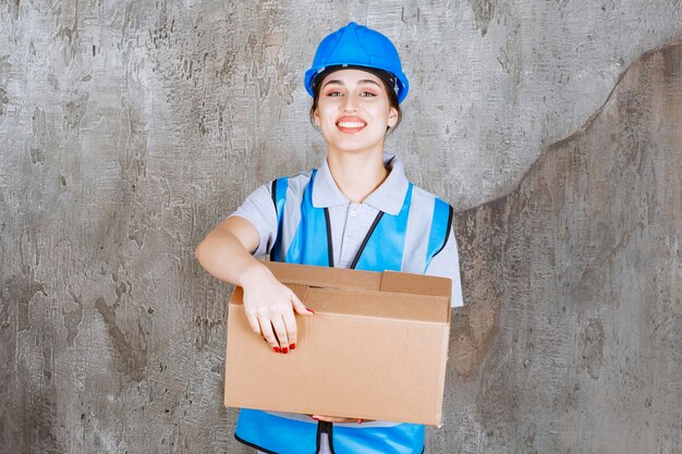 Free Photo female engineer in blue uniform and helmet holding a cardboard parcel.