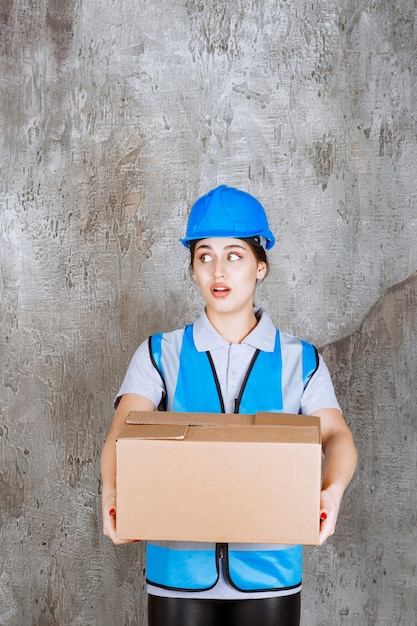 Free Photo female engineer in blue uniform and helmet holding a cardboard parcel. 