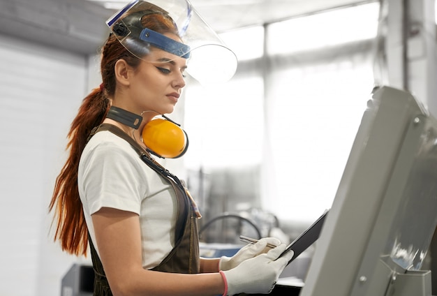 Female engineer in protective clothes working on factory.