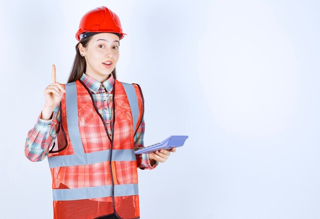 Female engineer in red helmet working on calculator and having an idea.