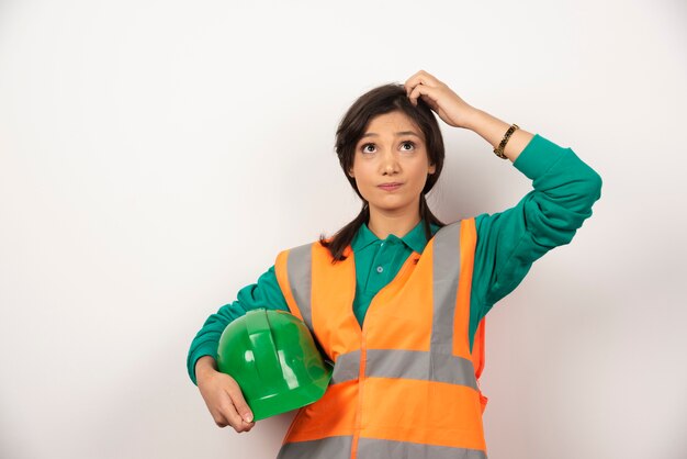 Female engineer scratching her head and holding a helmet on white background.