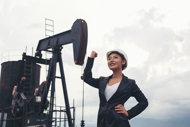 Free photo female engineer standing with working oil pumps with a white sky .