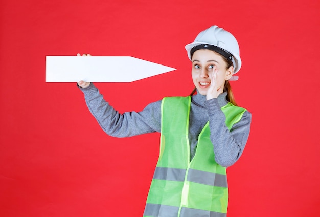 Free Photo female engineer with white helmet holding an arrow pointing right and looks confused. 